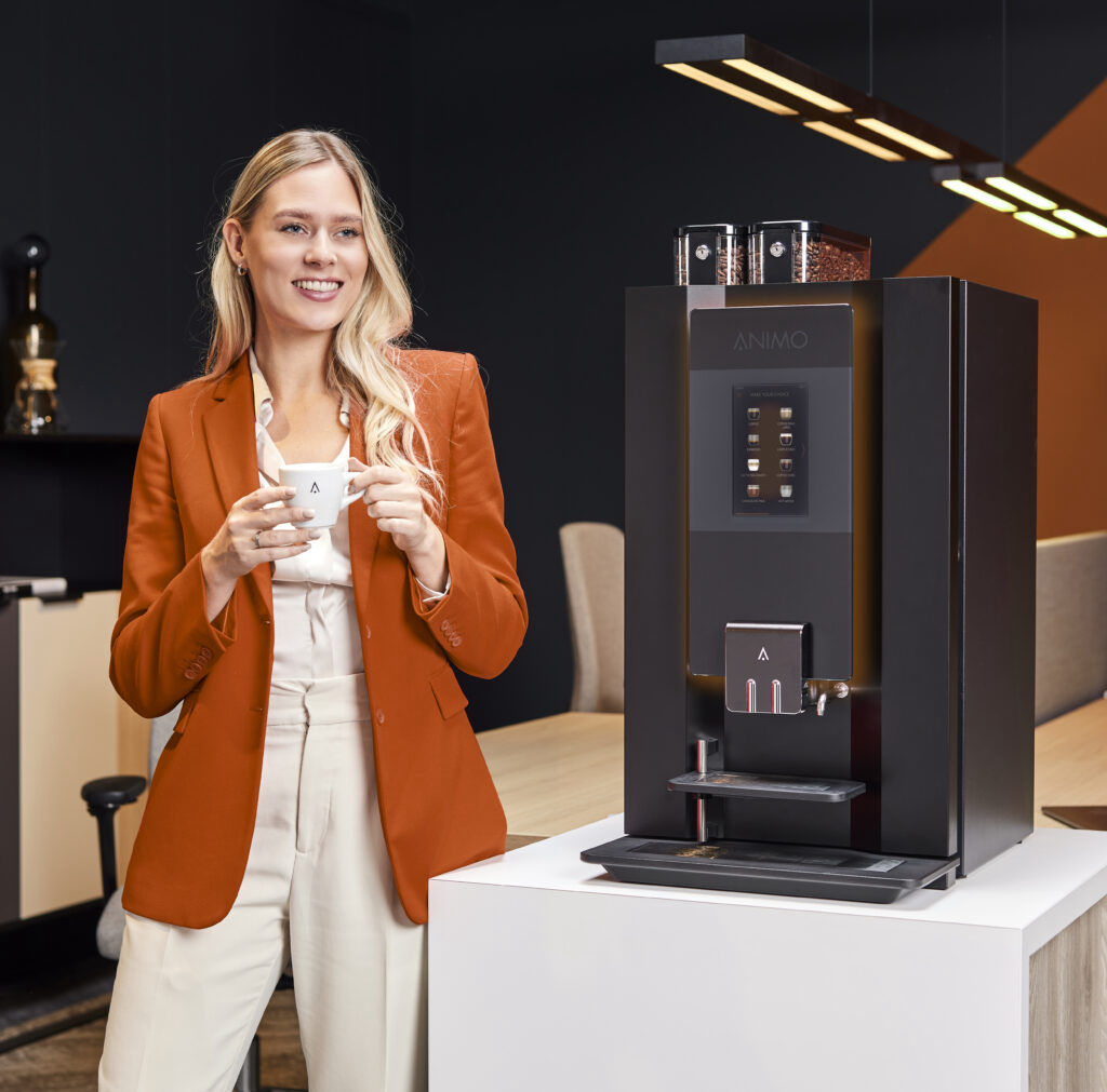 Frau steht vor Kaffeemaschine mit Tasse in den Händen