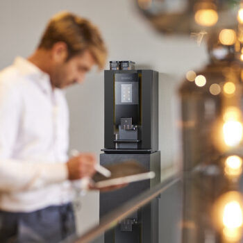 Mann unscharf am Tablet - im Hintergrund die Kaffeemaschine